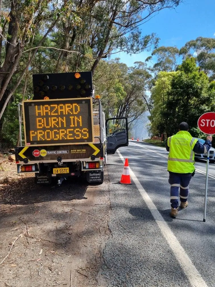 A traffic controller beside an SSTC message board reading HAZARD BURN IN PROGRESS
